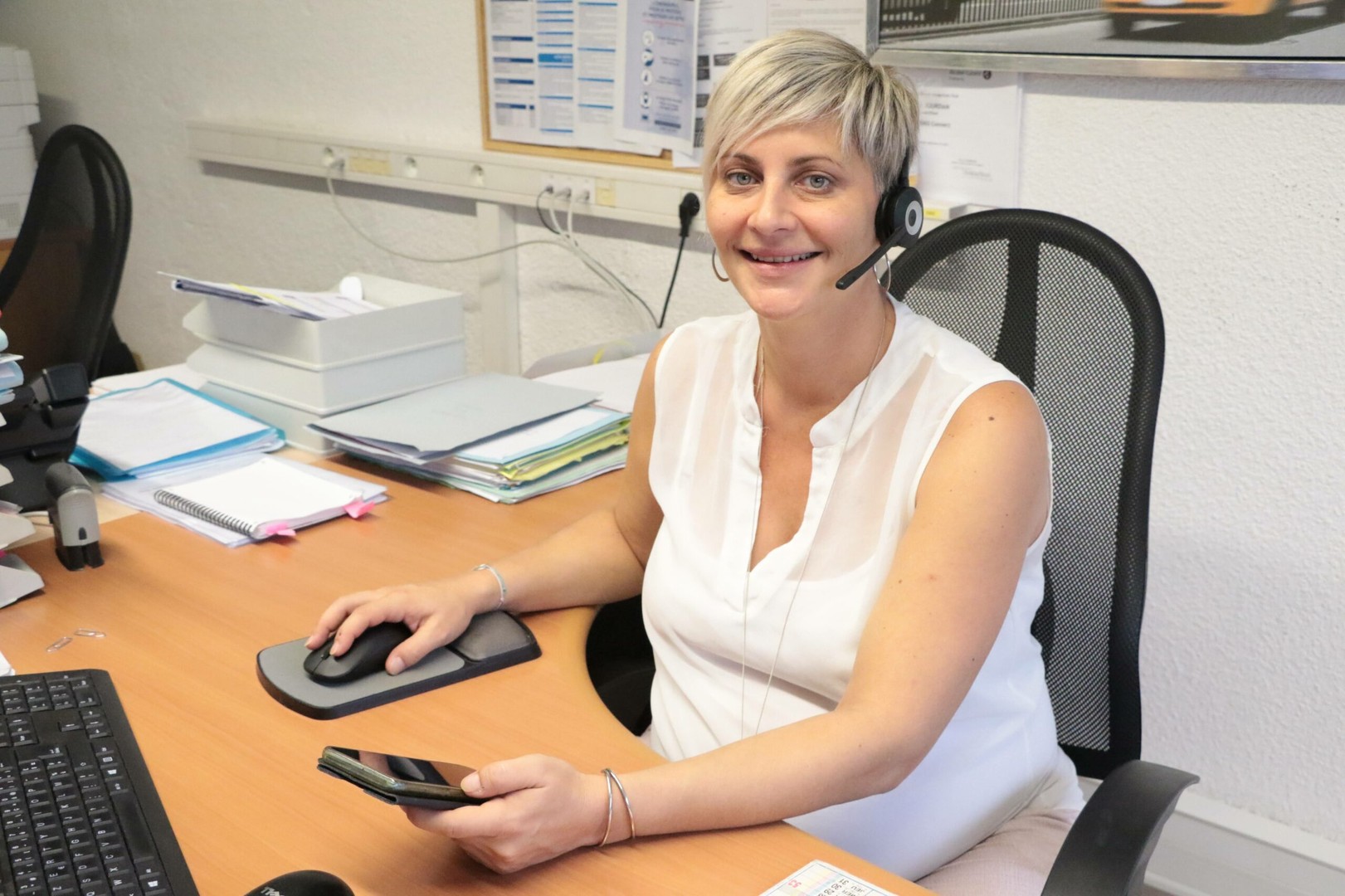 Une collaboratrice souriante avec casque assure le support téléphonique et informatique aux TPE et PME