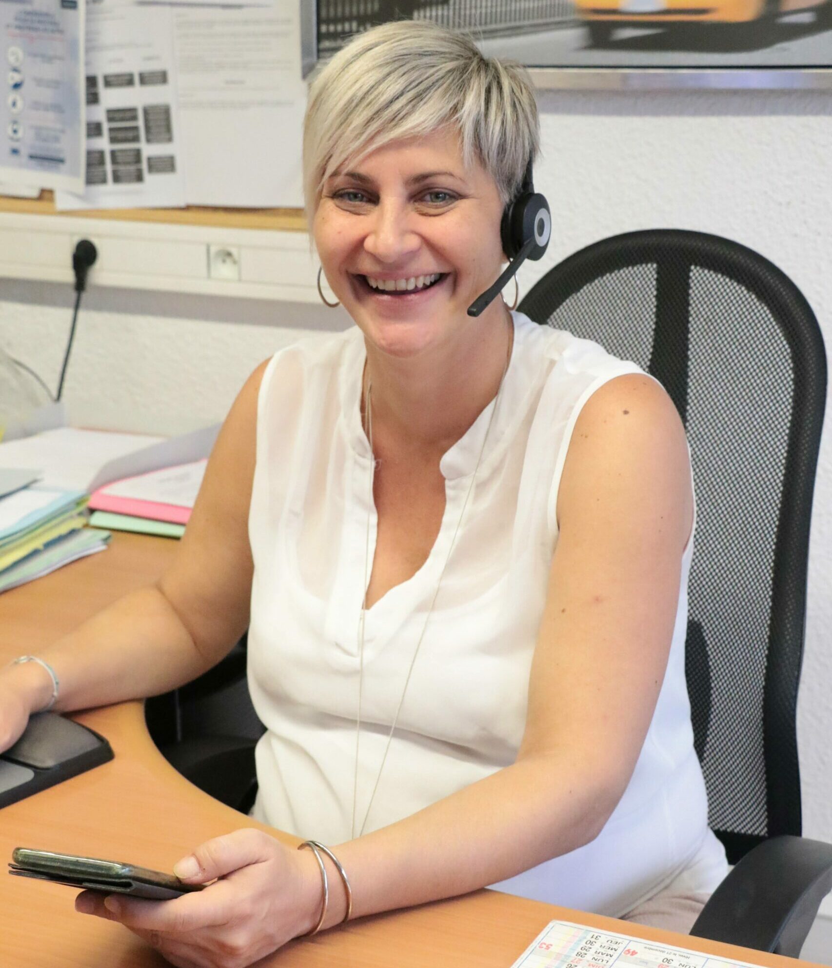 Une collaboratrice souriante avec casque assure le support téléphonique et informatique aux TPE et PME